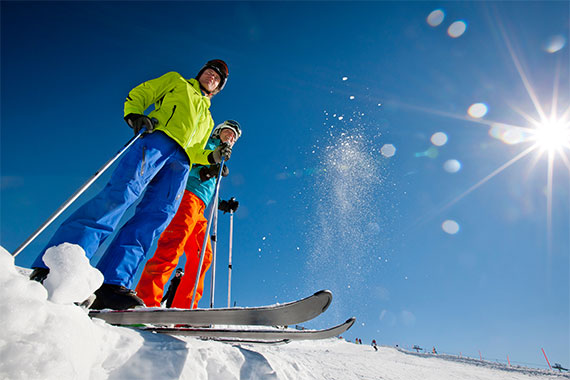 Zwei Skifahrer stehen auf der Piste und genießen den Ausblick auf die verschneite Bergwelt